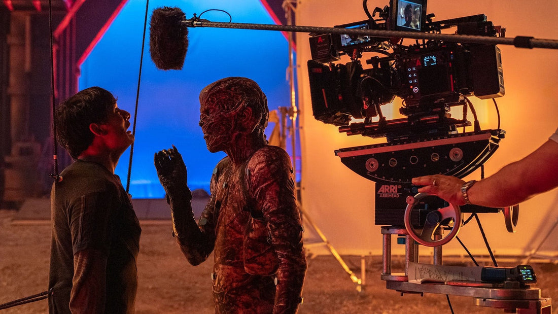 Sul set di Stranger Things: telecamera, asta del microfono e fondo blu davanti a un attore truccato da creatura