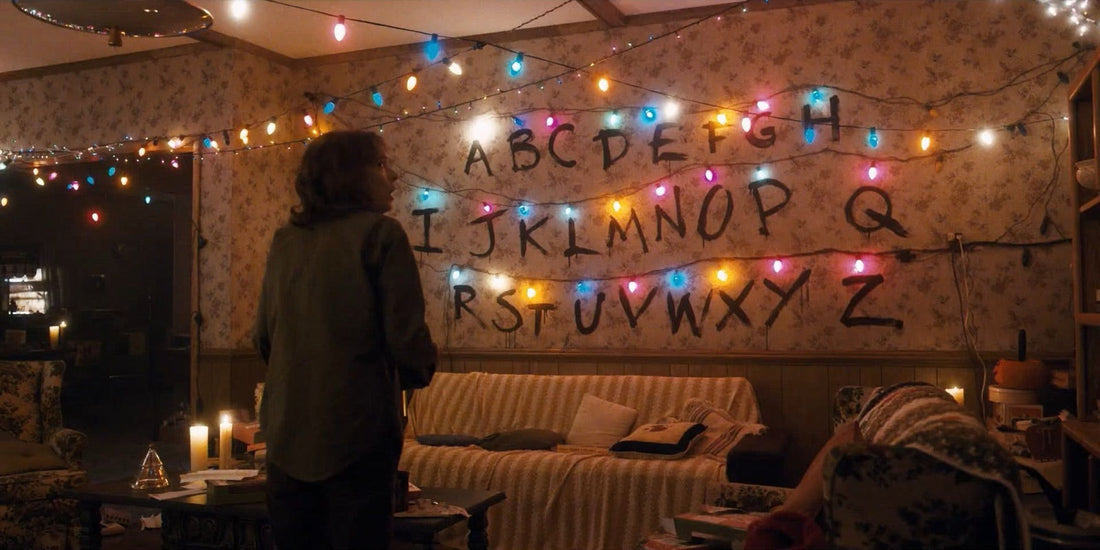 Joyce davanti al muro dell'alfabeto e alle sue ghirlande accese in Stranger Things