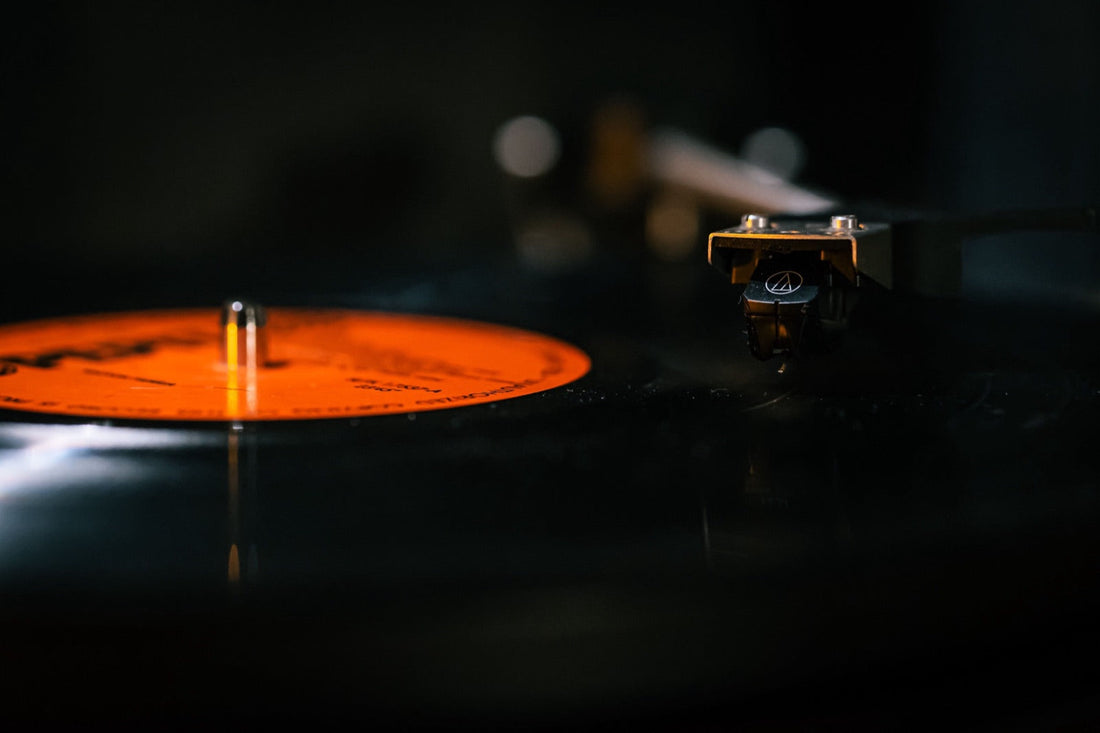 Un vinile gira sul giradischi, braccio appoggiato sul solco, riflessi aranciati nella penombra