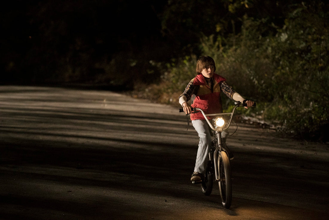 Will in bici, di notte, su una strada tra gli alberi, con il fanale acceso.