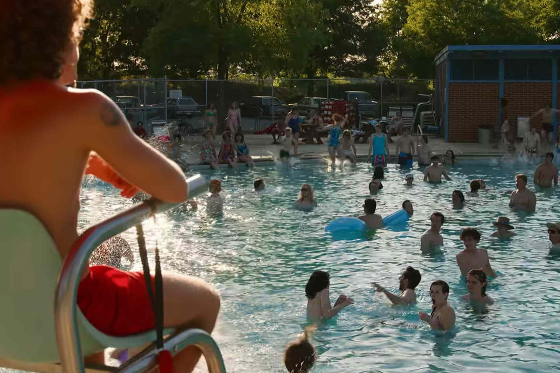 Piscina comunale affollata, d'estate, con la sedia del bagnino in primo piano.
