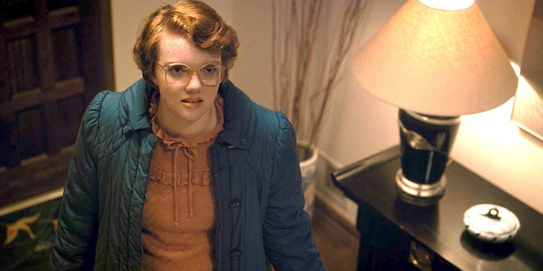 Shannon Purser nei panni di Barbara Holland, occhiali e cappotto blu, in un ingresso.